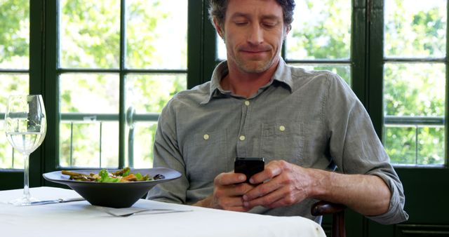Man sitting at restaurant table using smartphone. Perfect for depicting solo dining experiences, technology use in everyday life, or concepts of communication and connectivity.
