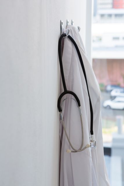 Laboratory coat and stethoscope hanging on wall hook in a medical setting. Ideal for illustrating healthcare environments, medical professions, and clinical settings. Useful for medical articles, healthcare blogs, and educational materials.