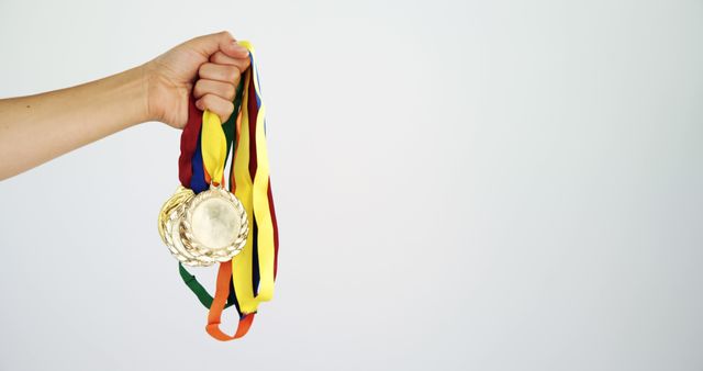 Hand holding several gold medals with colorful ribbons against plain background. Great for illustrating achievement, victory, and recognition in sports or other competitive fields. Perfect for use in promotional materials, award ceremonies, or motivational content.