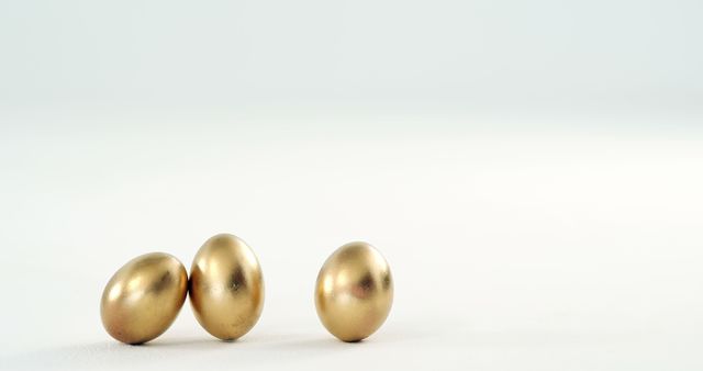 Three golden eggs are positioned closely together on a plain white background, with copy space. Their shiny surfaces suggest wealth or the concept of valuable opportunities.
