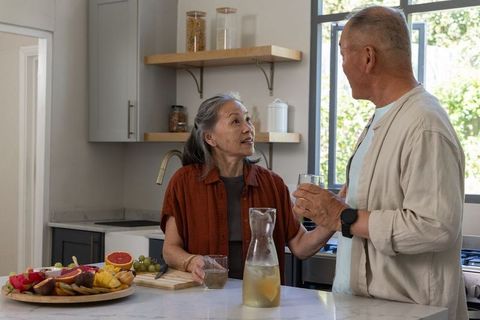 Senior asian couple chatting over refreshing drink in modern kitchen, healthy home moment together