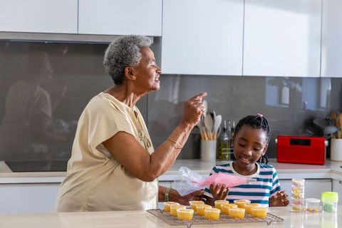 African american grandma teaching granddaughter cupcake decorating and frosting in kitchen