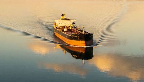 Oil tanker gliding through golden sunrise waters with mirror reflection and wake seascape