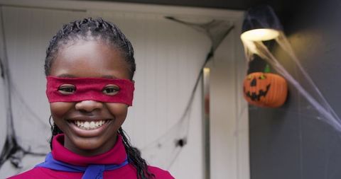 African American child smiling in red mask and blue cape on decorated porch for Halloween