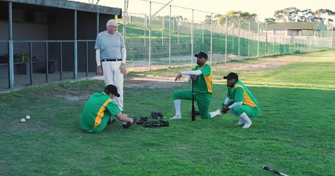 Senior coach guiding multiracial baseball players during relaxed outfield practice session