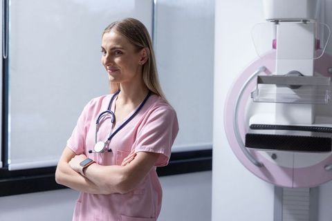 Confident mammography technologist in pink scrubs standing with arms crossed