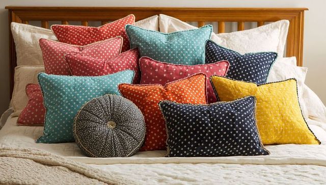 Stacking colorful polka dot throw pillows on bed with wooden slatted headboard and round bolster