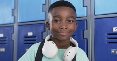 Confident African American Preteen Boy Wearing White Headphones by Blue School Lockers