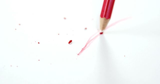 A red pencil breaks while writing, leaving a snapped tip and debris on a white surface, with copy space. It illustrates frustration or the concept of pressure leading to failure.