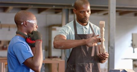 Carpentry mentor teaching apprentice examining turned wooden spindle in workshop