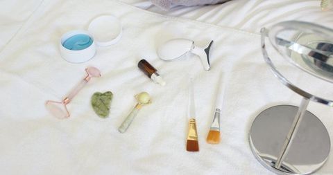 Skincare tools on white towel with jade roller, rose quartz gua sha, hydrogel eye patches