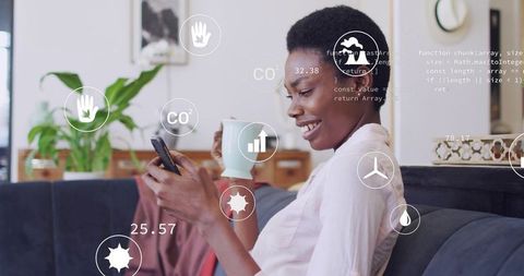 Smiling woman checking smartphone on couch holding mug with eco data and energy overlays