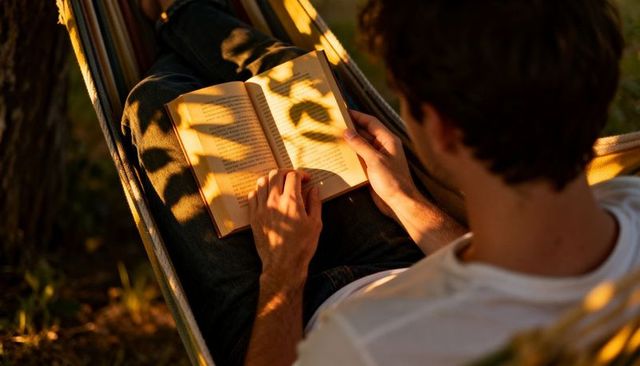 Young man reading in hammock at golden hour with warm sunlight and leaf shadows