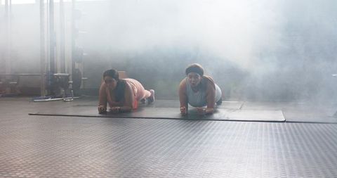 Diverse women holding planks on mats in hazy gym, building core strength and endurance