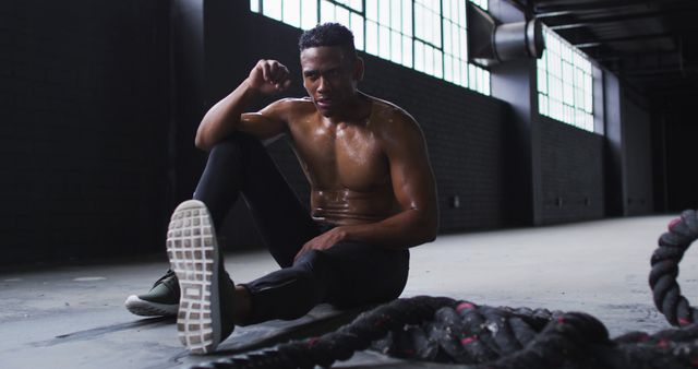 Shirtless african american man resting after battling ropes in an empty urban building. urban fitness and healthy lifestyle.
