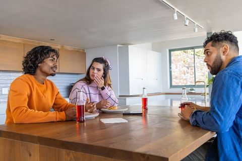 Multicultural friends chatting at kitchen island sipping red soda and eating pastries