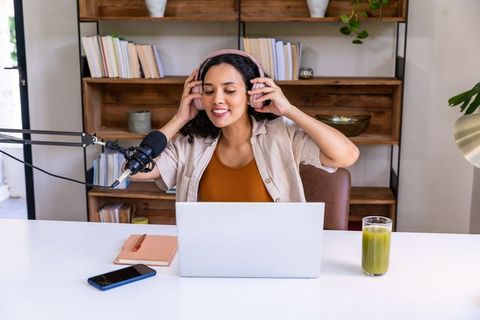 African american woman recording podcast from home office with laptop and boom microphone