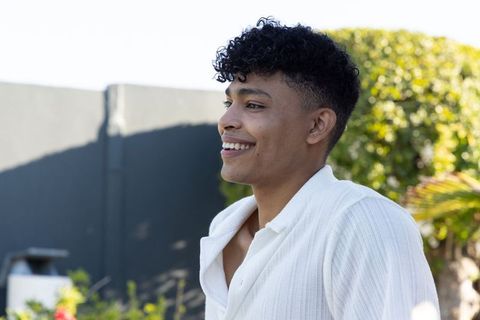 African man smiling outdoors in white textured shirt on sunny patio with green hedge