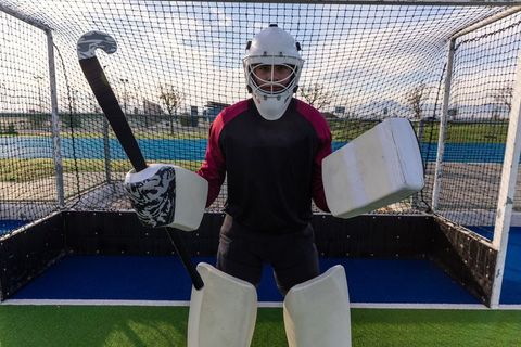 Field hockey goalkeeper standing ready with stick and protective gear