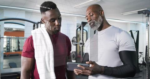 Personal trainer coaching client in gym while reviewing workout plan on smartphone