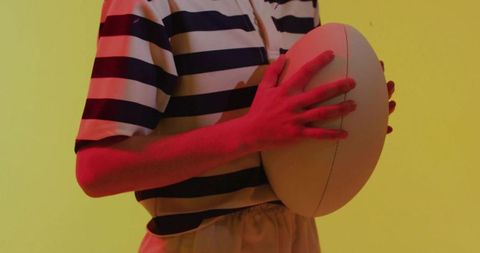 Adult female torso holding rugby ball in neon pink and yellow lighting, striped jersey