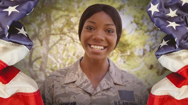 Close-up of a smiling African American female soldier dressed in uniform, outdoors and surrounded by American flags. Great for illustrating themes of patriotism, military service, celebrating national holidays like Independence Day, Veterans Day, or related to recruitment campaigns.