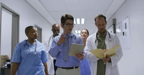Hospital medical team walking corridor discussing patient care, records and collaboration