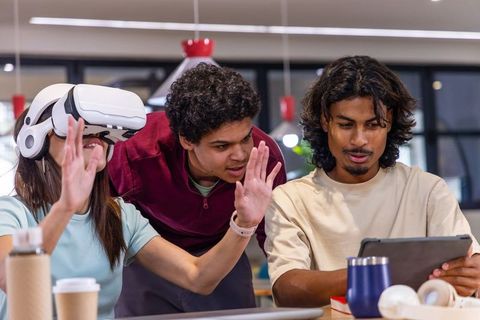 Multicultural students collaborating with VR headset and tablet in modern coworking space