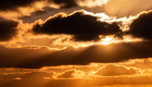 Golden sunbeams piercing layered clouds at sunset creating dramatic amber crepuscular rays