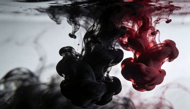 Duotone ink swirling in water black and red plumes backlit macro abstract art
