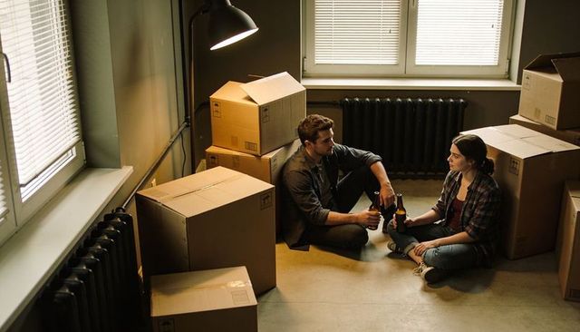 Young couple unpacking boxes in new apartment sharing beer during cozy move-in evening