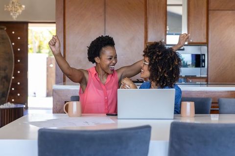 Diverse Women Celebrating Success Working Together at Kitchen Island with Laptop