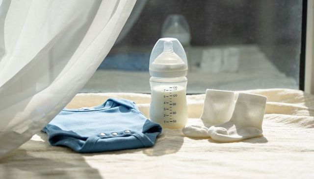 Sunlit newborn essentials basking in soft window light with blue onesie, bottle, socks