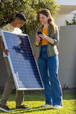 Young diverse team installing residential solar panel while checking smartphone data