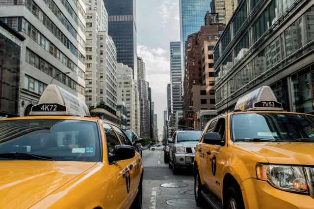 Busy city scene capturing multiple yellow taxis in Manhattan. Skyscrapers line the street, showcasing city life and urban atmosphere. Ideal for depicting transportation, urban lifestyle, travel destinations, or city infrastructure.
