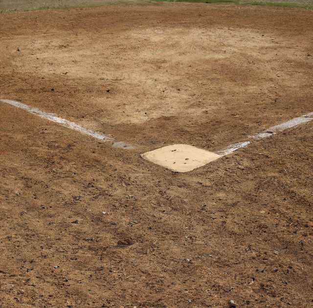 This image shows an empty baseball field with its focus on the home plate, located on a dirt infield. The absence of players and equipment creates a serene, ready-for-action atmosphere suitable for promoting upcoming games, camps, or any baseball-related events. It can also be used in sports magazines, blog posts, or educational materials discussing baseball.