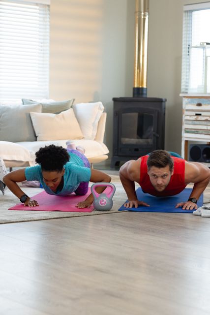Diverse couple performing push-ups on yoga mats in a cozy living room. Ideal for promoting home workouts, fitness routines, and spending quality time together. Useful for articles on healthy living, exercise at home, and couple activities.