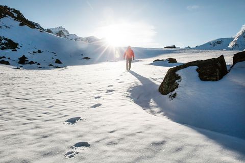 Person Hiking on Snow-Covered Mountain Against Bright Sun