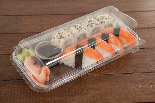 Nigiri and uramaki sushi kept with soy sauce in a plastic box on wooden table