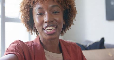 Young woman recording selfie video on smartphone smiling warmly in sunlit living room