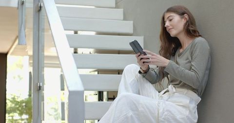 Relaxed Woman on Modern Staircase Using Foldable Smartphone Indoors