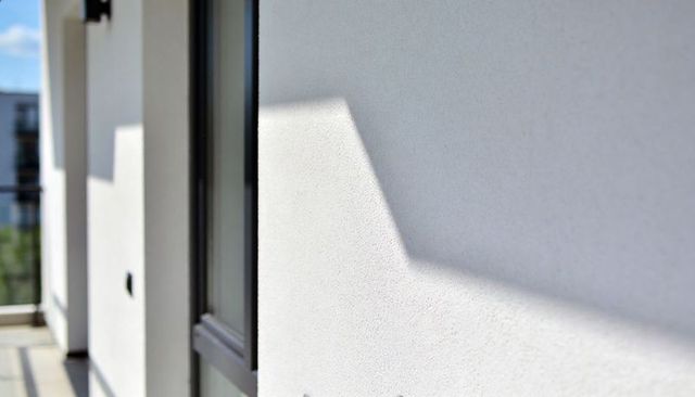 White plaster facade casting angular shadow on balcony with glass balustrade geometry