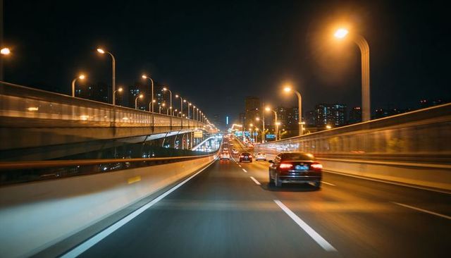 Night traffic flowing on elevated expressway toward illuminated urban skyline