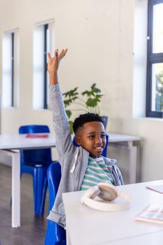 African american boy raising hand in classroom, confident student engaging in learning
