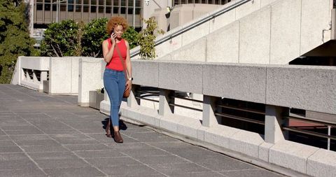 African american woman walking and talking on smartphone along urban concrete promenade