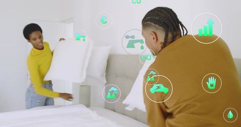 Young couple arranging pillows on bed with eco icons for sustainable home comfort and style
