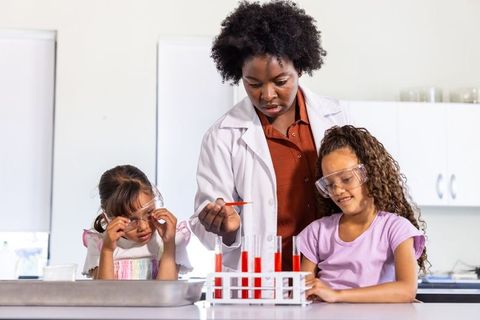 African american teacher guiding girls in safe science experiment with red test tubes