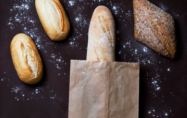 This stock photo captures a variety of artisanal bread displayed on a dark background with scattered flour for a rustic look. Ideal for use in bakery advertisements, food blogs, recipe books, or culinary themed websites. It showcases freshness and a home-baked texture, making it perfect for promoting baking products and services.