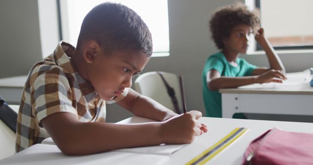 Image of focused biracial boy sitting at desk in classroom. primary school education and learning concept.