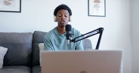 Young male podcaster recording from home studio speaking into microphone with laptop